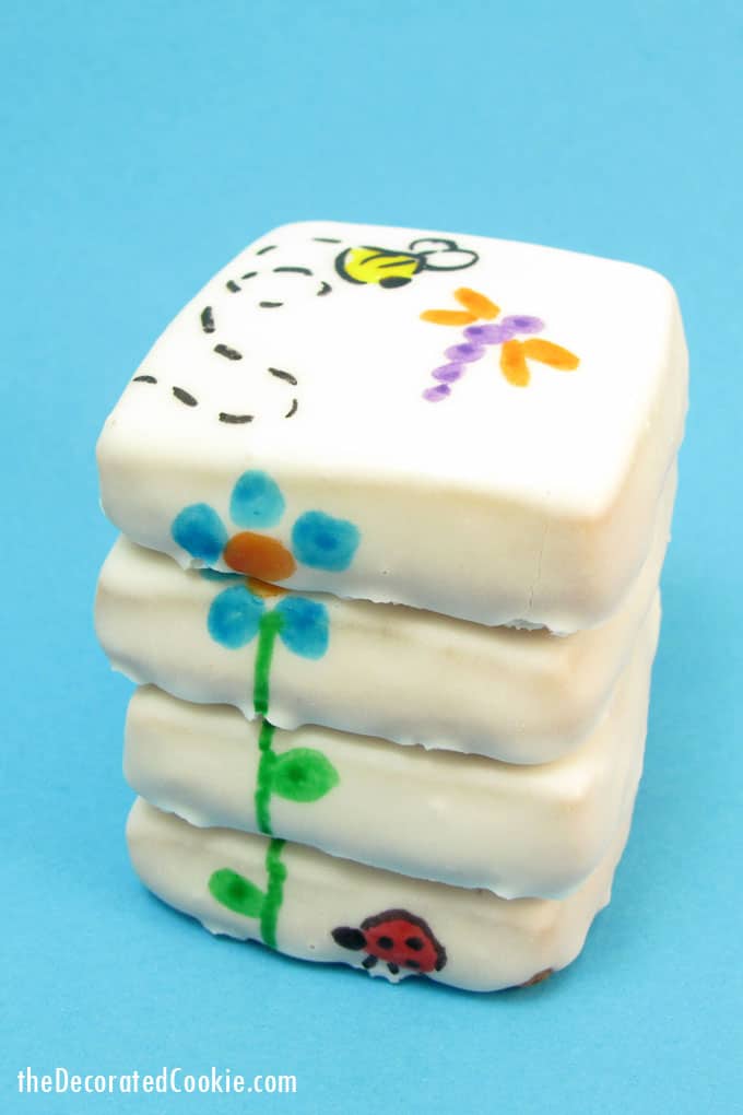 Stacked flower cookies for Spring with poured sugar icing and designs hand-drawn with food coloring pens.