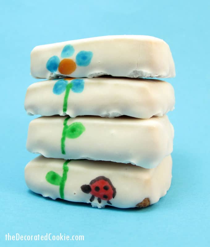 Stacked flower cookies for Spring with poured sugar icing and designs hand-drawn with food coloring pens.