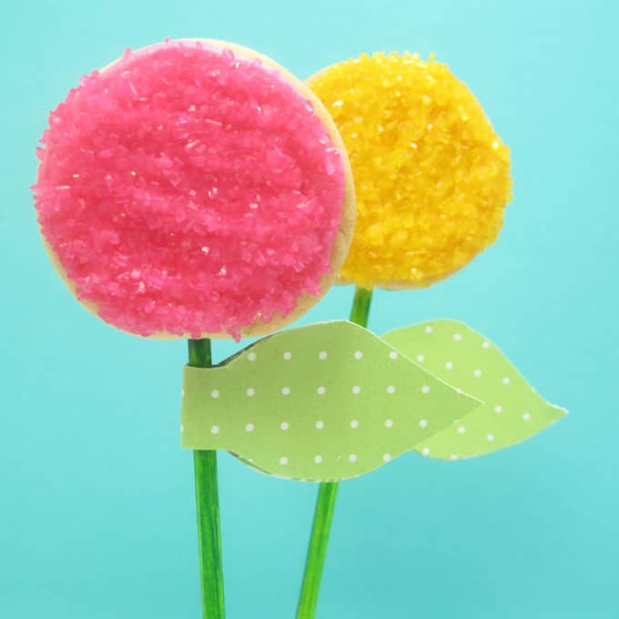 How to decorate easy flower cookie pops using sprinkles. Attach paper leaves to make place cards or party favors for a spring or garden party.