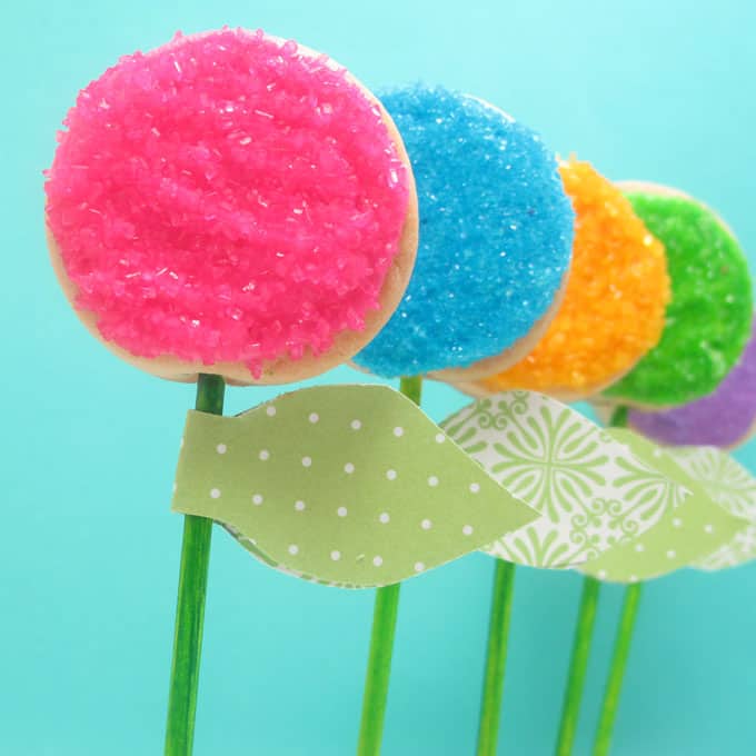 How to decorate easy flower cookie pops using sprinkles. Attach paper leaves to make place cards or party favors for a spring or garden party.