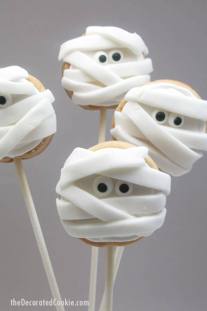 Halloween mummy cookies on a stick: Simple iced cookie pops topped with strips of fondant and candy eyes becomes spooky mummy cookies!