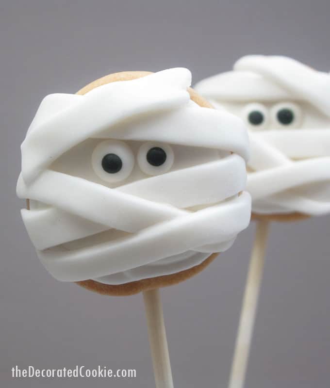 Halloween mummy cookies on a stick: Simple iced cookie pops topped with strips of fondant and candy eyes becomes spooky mummy cookies!