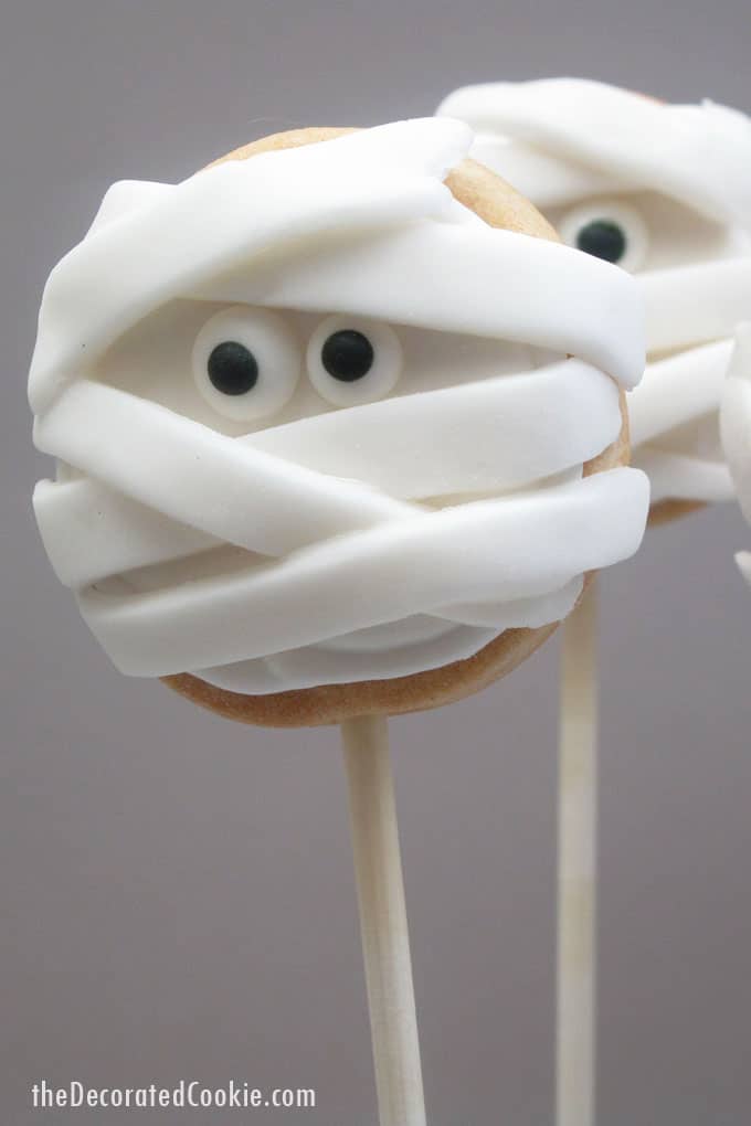 Halloween mummy cookies on a stick: Simple iced cookie pops topped with strips of fondant and candy eyes becomes spooky mummy cookies!