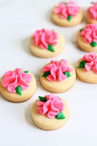 MINI ROSE COOKIES -- Simple buttercream frosting flowers on bite-size cut-out sugar cookies are a pretty and pink Valentine's Day cookie idea. #valentinesday #cookiedecorating #rosecookies #flowers #pink #frosting